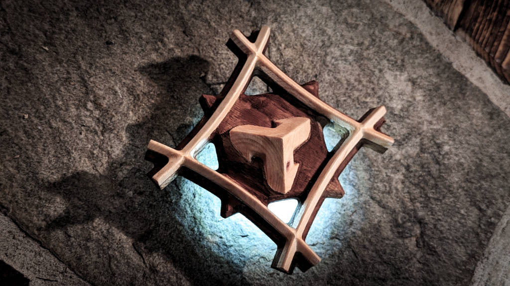 Photo of a wooden art object. It shows a framed cube with the tip pointing upwards with blue background lighting.