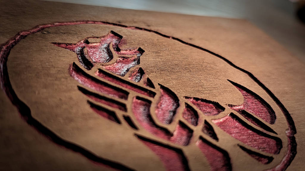 Closeup of a wolf logo as a red coloured engraving in wood.